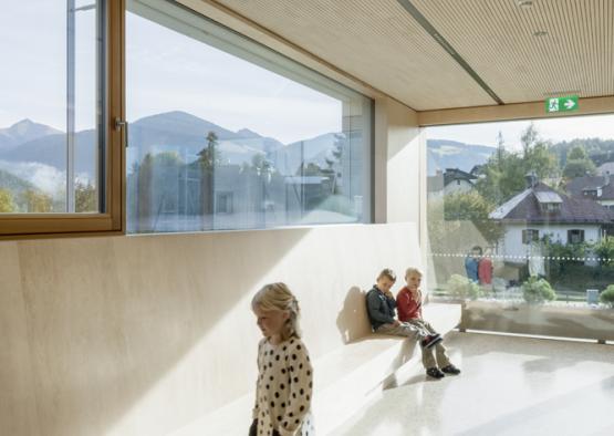 a group of kids sitting on a bench in a room with large windows