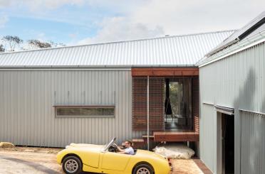 a man driving a yellow convertible car in front of a house